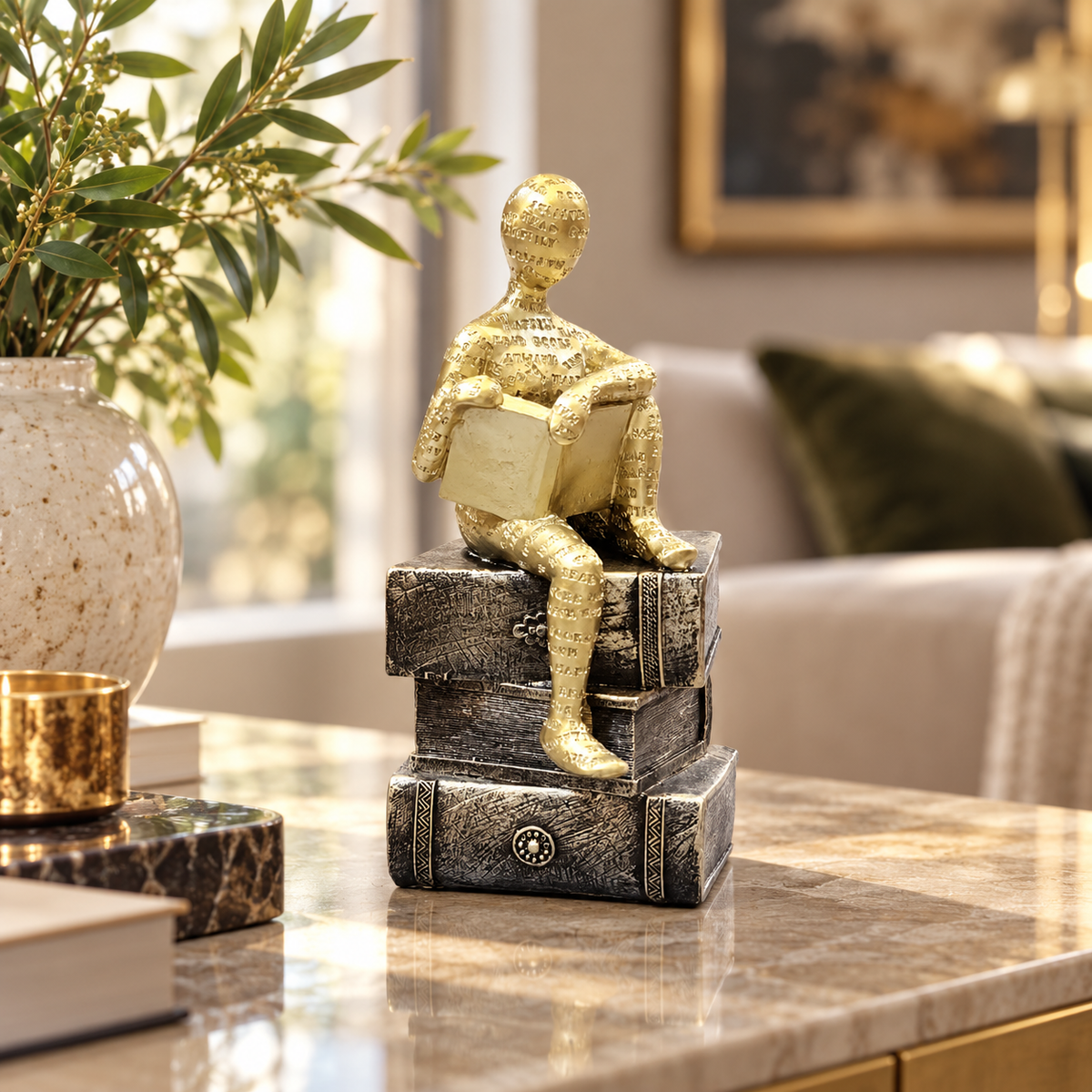 Gold reader sculpture seated on decorative books