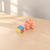 White-framed turning cube and pink-yellow articulated puzzle toy on a wooden desk