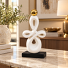 White symmetrical knot ceramic sculpture with gold sphere on black base