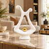 White twin figure ceramic sculpture with central gold sphere on black base